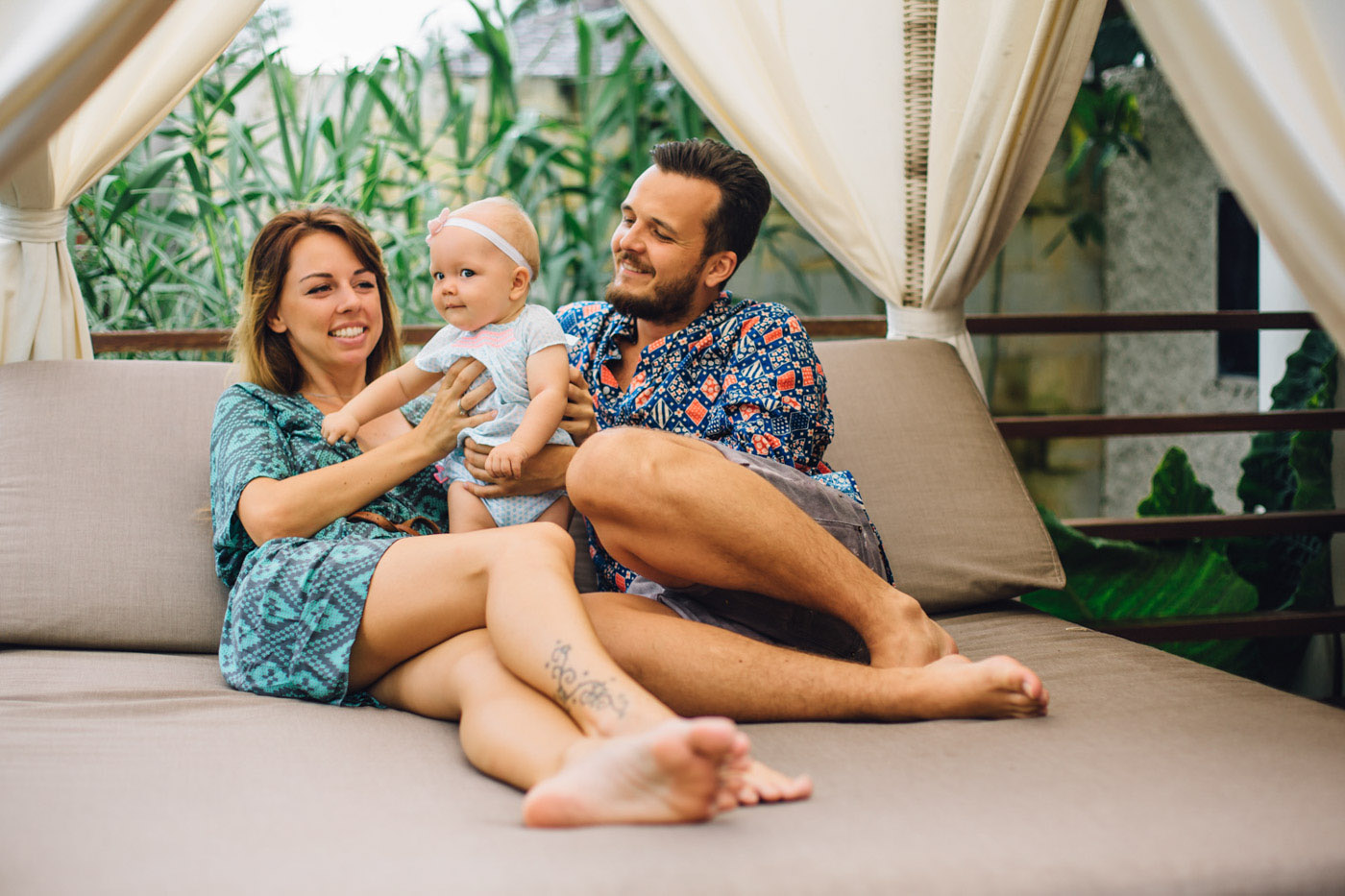 
Mom and dad playing with the baby, the kid is smiling, laughing and posing on the camera. The girl has a tattoo on her leg